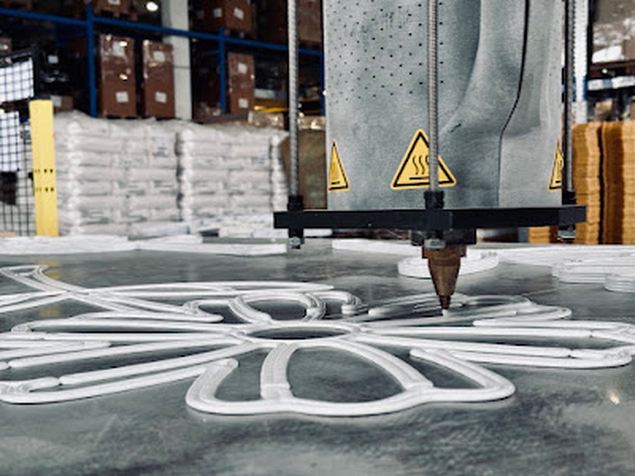 Detail trysky 3D tiskárny při výrobě bílé konstrukce ve tvaru květiny.